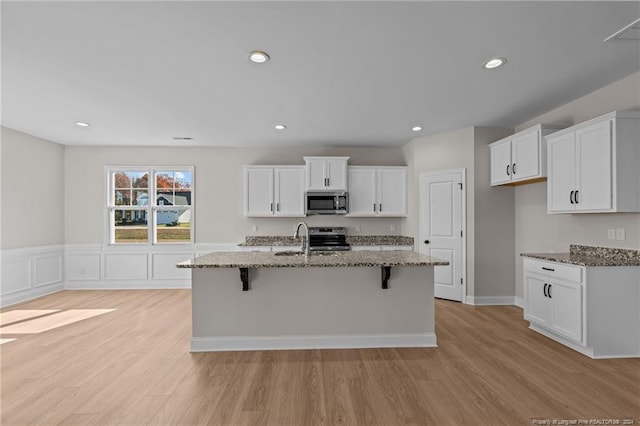 kitchen with white cabinets, stainless steel appliances, a kitchen island with sink, and dark stone counters