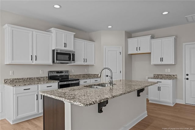 kitchen with light wood-type flooring, stainless steel appliances, sink, white cabinets, and an island with sink