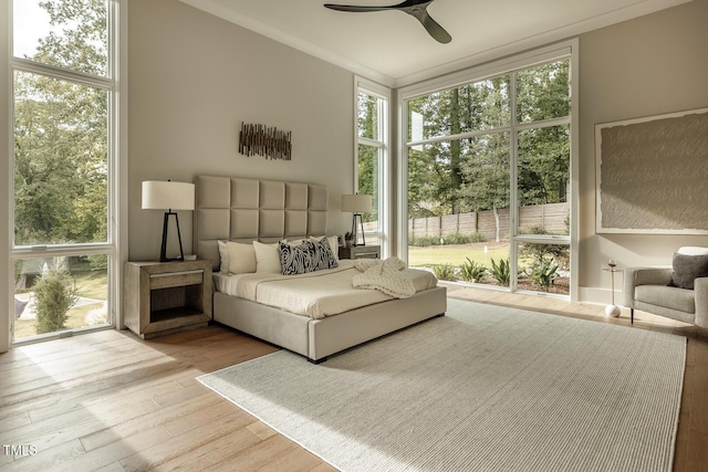 bedroom featuring light wood-type flooring, multiple windows, ornamental molding, and ceiling fan