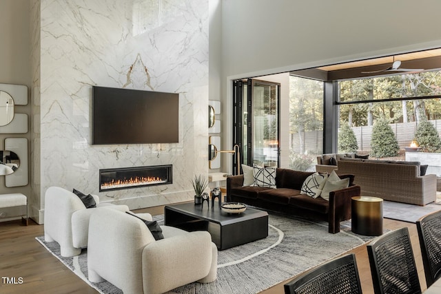 living room featuring ceiling fan, wood-type flooring, a high ceiling, and a high end fireplace