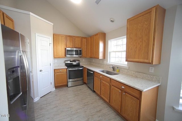 kitchen with vaulted ceiling, appliances with stainless steel finishes, sink, and light stone counters