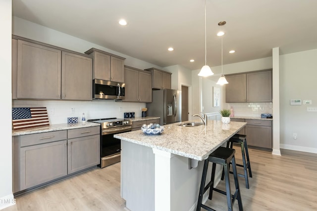 kitchen with sink, stainless steel appliances, light hardwood / wood-style floors, decorative light fixtures, and a breakfast bar