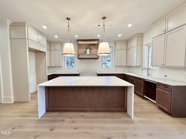 kitchen featuring light hardwood / wood-style floors, black dishwasher, decorative light fixtures, a kitchen island, and sink