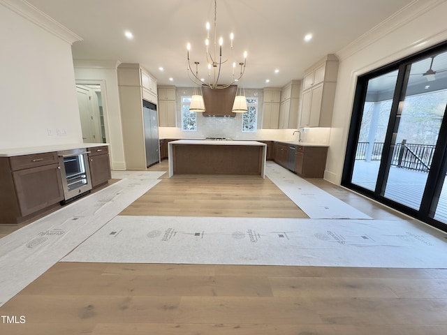 kitchen featuring built in fridge, hanging light fixtures, a center island, and crown molding