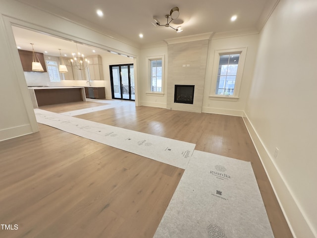 unfurnished living room featuring french doors, ornamental molding, a notable chandelier, hardwood / wood-style flooring, and a tiled fireplace