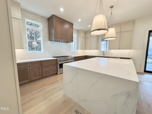 kitchen with decorative light fixtures, a center island, sink, range with two ovens, and light stone counters