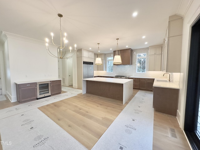 kitchen featuring a spacious island, a notable chandelier, beverage cooler, hanging light fixtures, and light hardwood / wood-style flooring