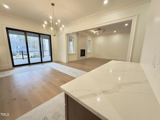 kitchen with pendant lighting, a large fireplace, light wood-type flooring, light stone countertops, and ornamental molding