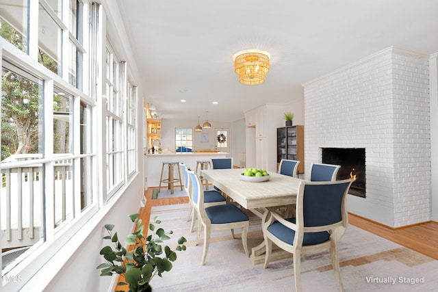 dining area with crown molding, light wood-type flooring, and a brick fireplace