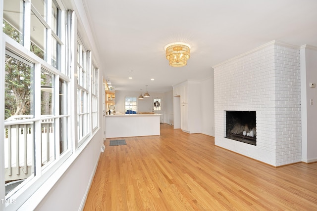 unfurnished living room featuring a brick fireplace, light hardwood / wood-style floors, crown molding, and an inviting chandelier