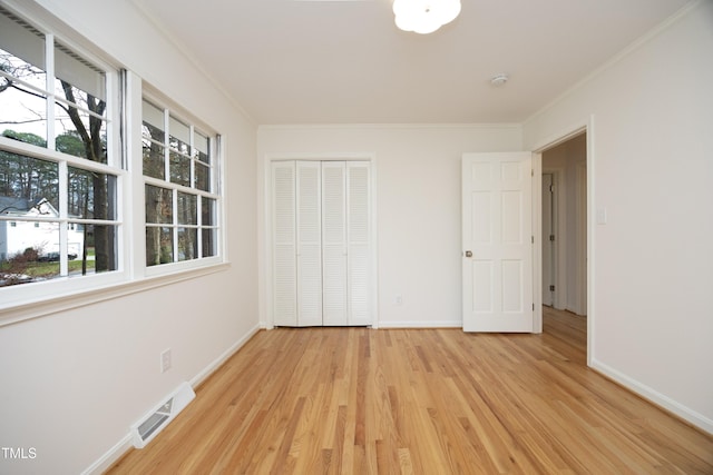 unfurnished bedroom featuring crown molding, light wood-type flooring, multiple windows, and a closet