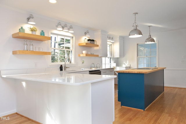 kitchen featuring pendant lighting, sink, kitchen peninsula, light wood-type flooring, and white cabinetry