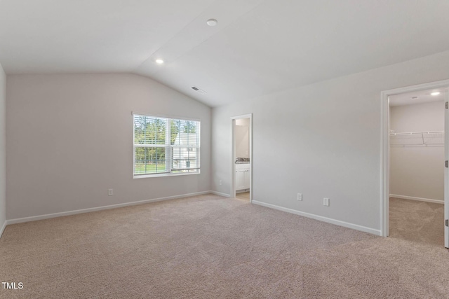 unfurnished bedroom featuring lofted ceiling, ensuite bathroom, a walk in closet, light colored carpet, and a closet