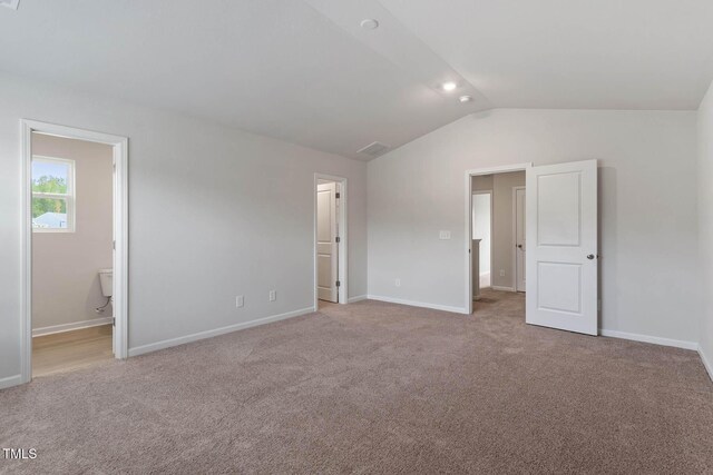 unfurnished bedroom featuring light carpet, ensuite bathroom, and vaulted ceiling