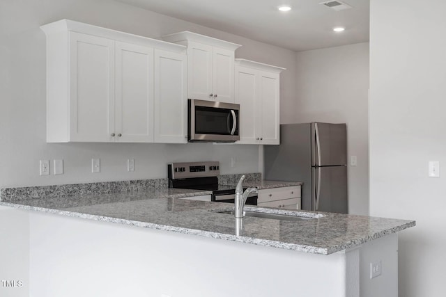 kitchen featuring white cabinets, appliances with stainless steel finishes, kitchen peninsula, and light stone counters