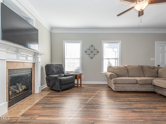 living room with dark wood-style floors, a tiled fireplace, ornamental molding, a ceiling fan, and baseboards