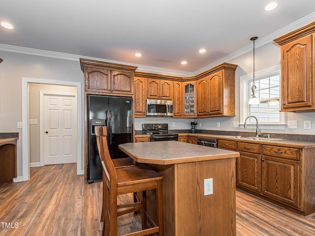 kitchen featuring glass insert cabinets, brown cabinets, a center island, black appliances, and a sink