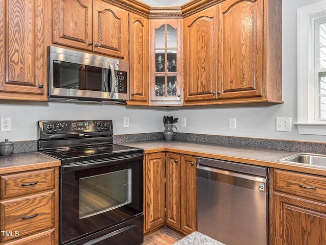 kitchen featuring brown cabinetry, glass insert cabinets, stainless steel appliances, and a sink