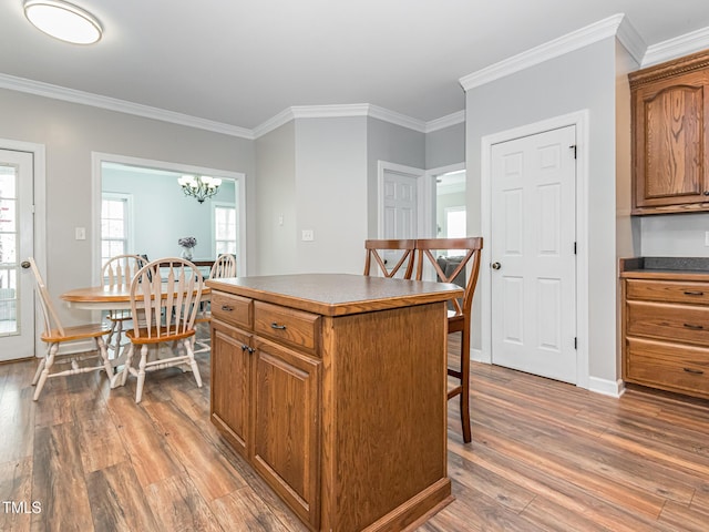 kitchen with brown cabinetry, dark countertops, wood finished floors, a center island, and crown molding