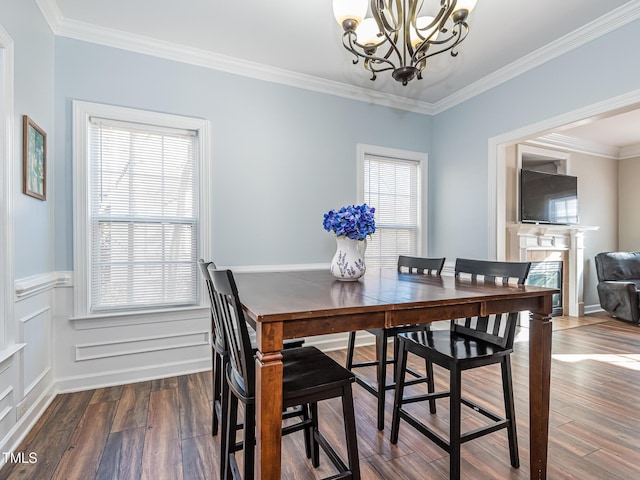 dining area featuring dark wood-style flooring, a notable chandelier, a decorative wall, ornamental molding, and wainscoting