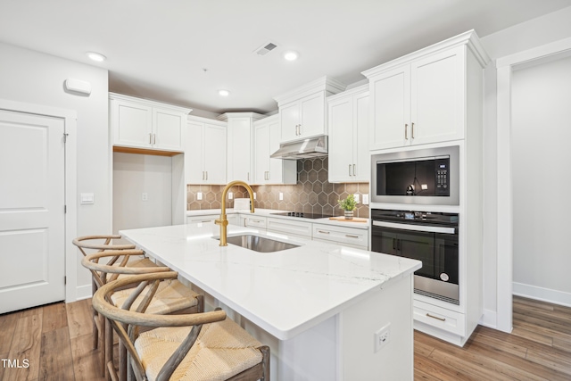 kitchen with a kitchen island with sink, sink, black appliances, and light wood-type flooring