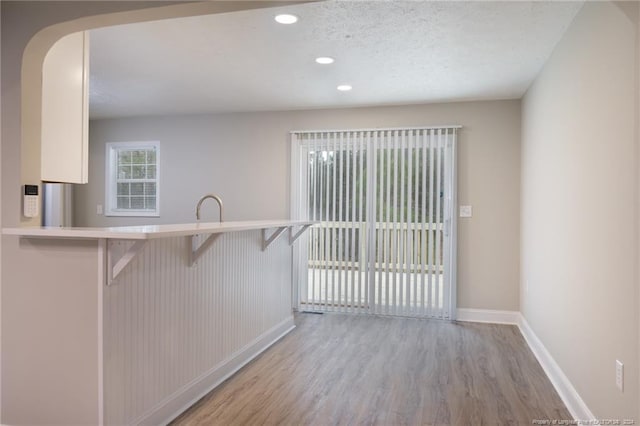 kitchen with light wood-type flooring, a kitchen breakfast bar, a textured ceiling, recessed lighting, and baseboards