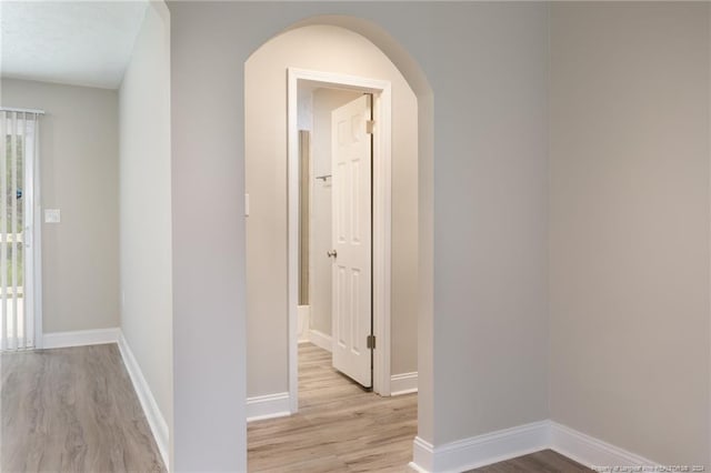 hall with arched walkways, light wood-type flooring, and baseboards