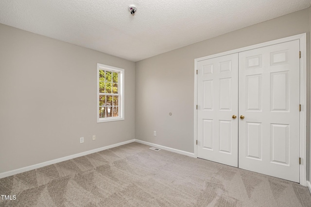 unfurnished bedroom with light colored carpet, a textured ceiling, and a closet