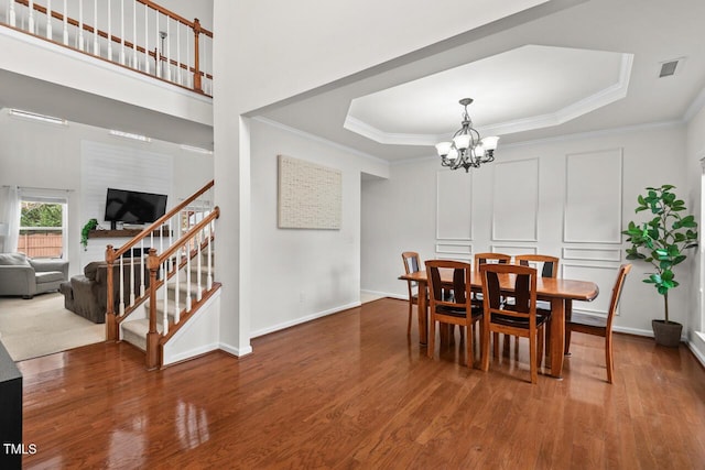 dining room with a chandelier, hardwood / wood-style flooring, a raised ceiling, and crown molding