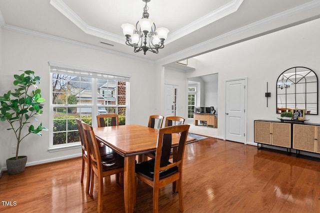 dining space with a raised ceiling, crown molding, hardwood / wood-style flooring, and an inviting chandelier