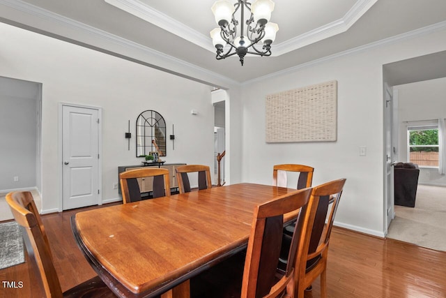 dining area with a tray ceiling, wood-type flooring, ornamental molding, and an inviting chandelier