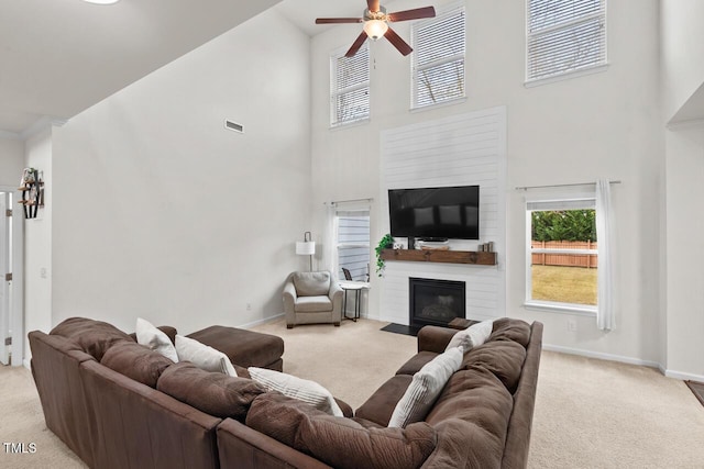 carpeted living room featuring ceiling fan, a fireplace, and a towering ceiling