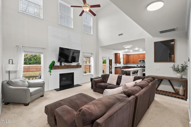 living room with ceiling fan, a towering ceiling, and light colored carpet