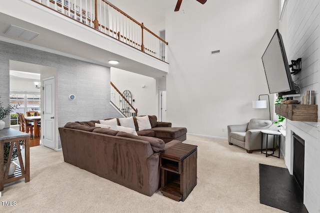 living room featuring ceiling fan, light colored carpet, a towering ceiling, and ornamental molding