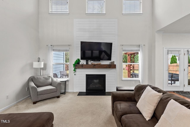 carpeted living room featuring a towering ceiling and a large fireplace