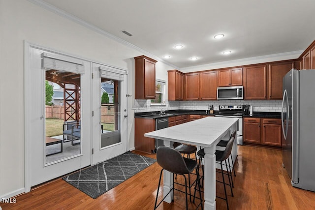 kitchen featuring appliances with stainless steel finishes, dark wood-type flooring, crown molding, and a kitchen breakfast bar