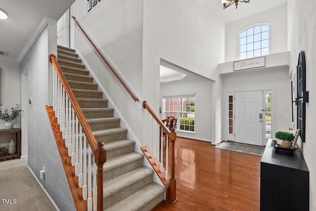 entryway with ornamental molding, a towering ceiling, wood-type flooring, and a notable chandelier