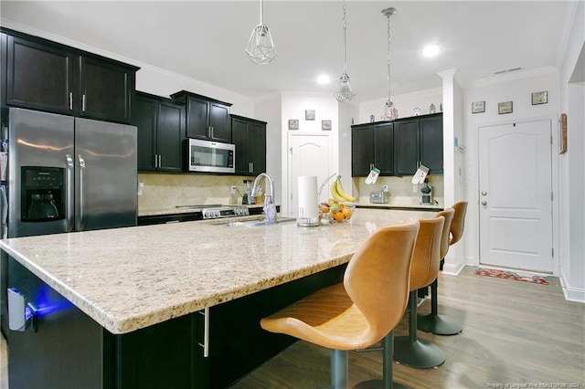 kitchen featuring pendant lighting, a center island with sink, sink, tasteful backsplash, and stainless steel appliances