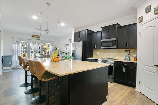 kitchen featuring pendant lighting, a center island with sink, crown molding, appliances with stainless steel finishes, and light hardwood / wood-style floors