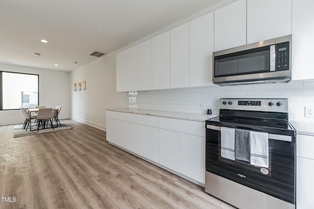 kitchen featuring white cabinets, light stone countertops, tasteful backsplash, light hardwood / wood-style floors, and stainless steel appliances