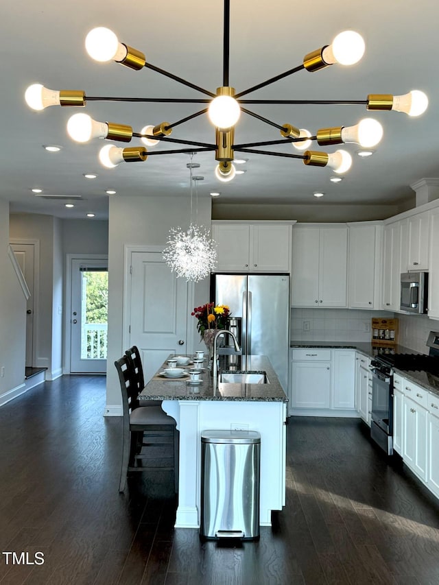 kitchen featuring appliances with stainless steel finishes, white cabinetry, dark stone counters, and an island with sink