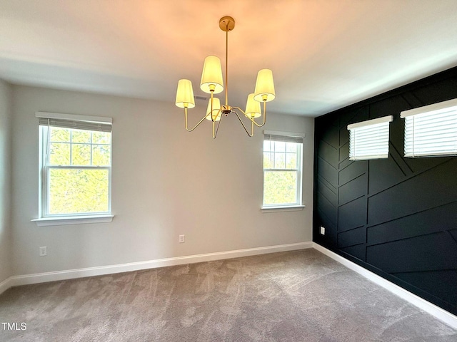 carpeted empty room with a healthy amount of sunlight and a notable chandelier