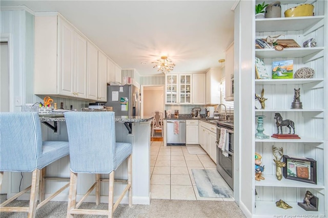 kitchen featuring appliances with stainless steel finishes, sink, a breakfast bar area, white cabinets, and dark stone counters