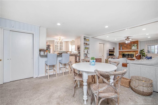 carpeted dining space featuring crown molding, ceiling fan, sink, and a brick fireplace