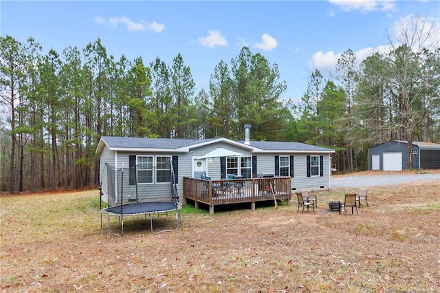 back of house with a garage, a deck, a trampoline, and an outbuilding