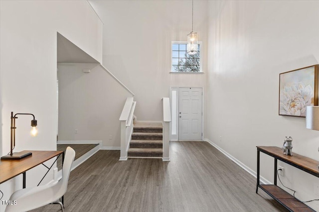 entrance foyer featuring baseboards, wood finished floors, stairs, a high ceiling, and a chandelier