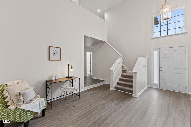 entrance foyer with a notable chandelier, a high ceiling, wood finished floors, baseboards, and stairs