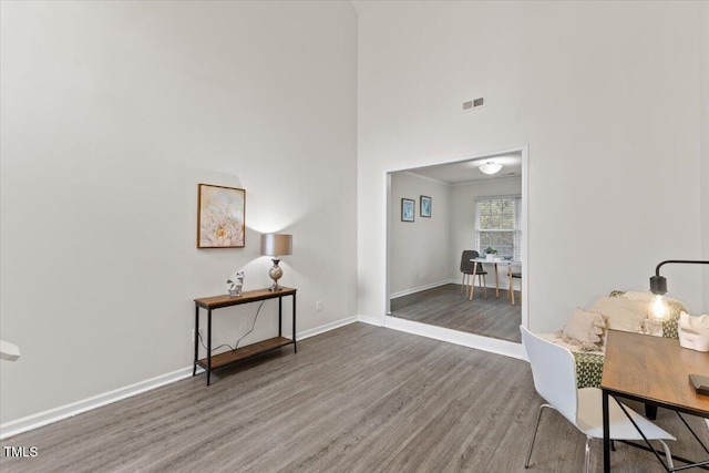 interior space with a high ceiling, wood finished floors, visible vents, and baseboards