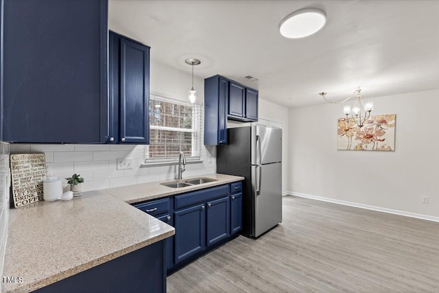 kitchen with blue cabinets, a sink, light wood-style floors, freestanding refrigerator, and decorative backsplash