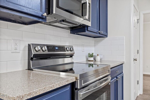 kitchen with blue cabinets, stainless steel appliances, wood finished floors, light countertops, and backsplash